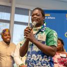 Diamond Suma stands in front of four Mandela Washington Fellows and speaks into a microphone. Behind them is a large sign with the UC Davis and UC Davis Global Affairs logos.