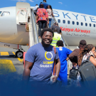 Roy Akumu smiles while wearing a UC Davis Global Affairs shirt in front of a Kenya Airways plane