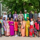 25 Mandela Washington Fellows and two administrators stand in two rows under a large tree outside the International Center to the left of the photo. The fellows all wear colorful traditional dress from their African nations.