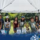 Group of volunteers under white canopy by lake with outreach table and Global Aggies logo