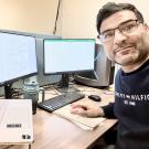 Dr. Ganji sits at a desk surrounded by two monitors and laptop and looks at the camera