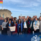 A group of people smile at the camera with a German flag flying in the background. A Global Aggies overlay covers the bottom of the photo.