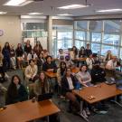 Students sit around their desk smiling for the camera.