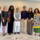 Group of 11 diverse adults in business-casual attire standing indoors, smiling
