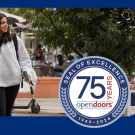 Two students walking on the UC Davis campus with an round seal that says Seal of Excellence 75 Years Open Doors 1949-2024