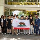 A group of students from Korea University and UC Davis faculty and staff hold up a California flag in front of the UC Davis International Center