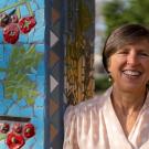 Wolf Prize recipient Pam Ronald outside Robbins Hall, leaning against pillar decorated with a ceramic mosaic mural. Pam has short light brown hair and wears a light pink blouse with cream polka dots.