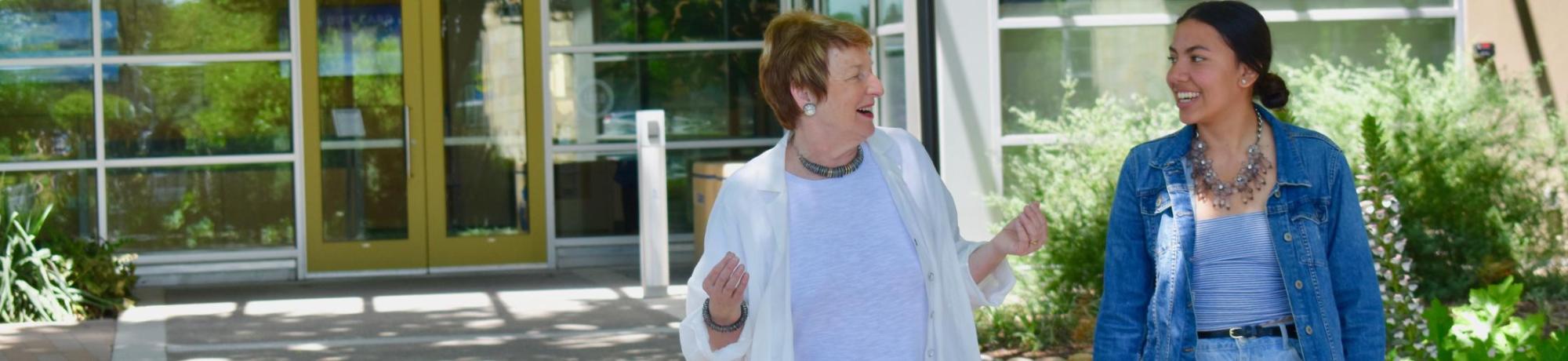 Two college students walking on campus, smiling, man in white hoodie and woman in denim jacket