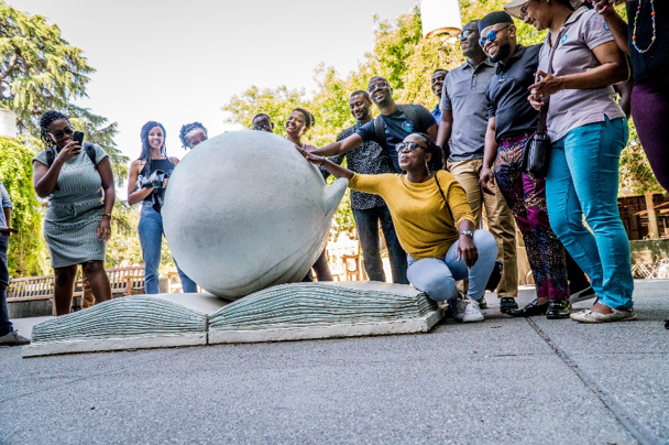 a group of adults rubbing a statue of a head in a book