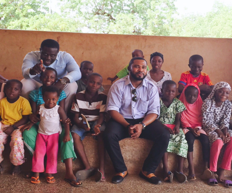 two men sitting with a group of children and a cement bench